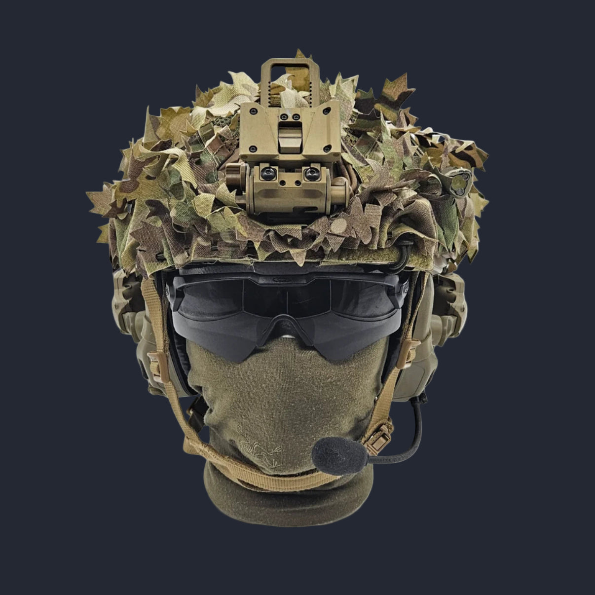 A camouflaged paintball helmet with a scrim visor and a radio attached.
