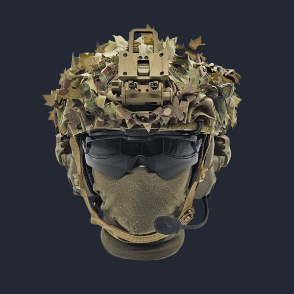 A camouflaged paintball helmet with a scrim visor and a radio attached.